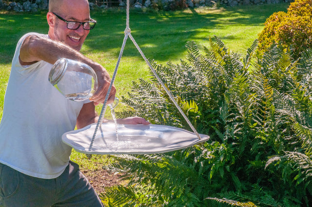 Peter Souza Jr. pouring water into a white ceramic hanging bird bath, J Schatz
