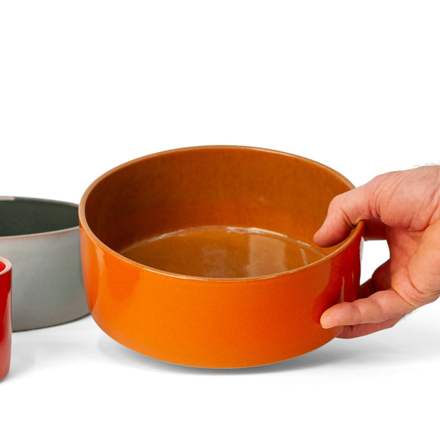 Fire orange ceramic Utilità bowl held to show the glossy interior, J Schatz.